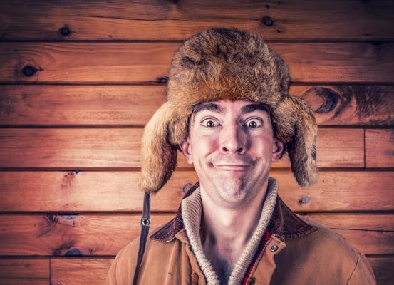 un hombre con sonrisa boba con un gorro de piel, al fondo una pared de madera